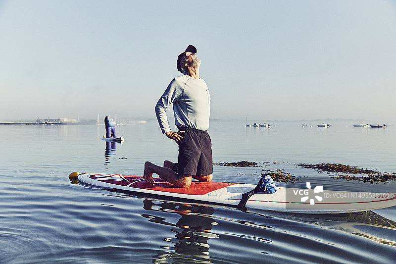 在雾中日出时分，桨板冲浪者以瑜伽姿势保持平衡图片素材