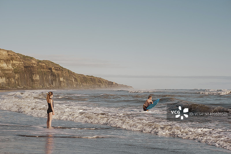 在海滩上拿着趴板和女孩在水里的男孩图片素材