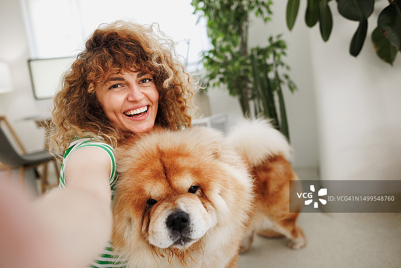 笑容甜美的女人在家与可爱的松狮犬自拍图片素材