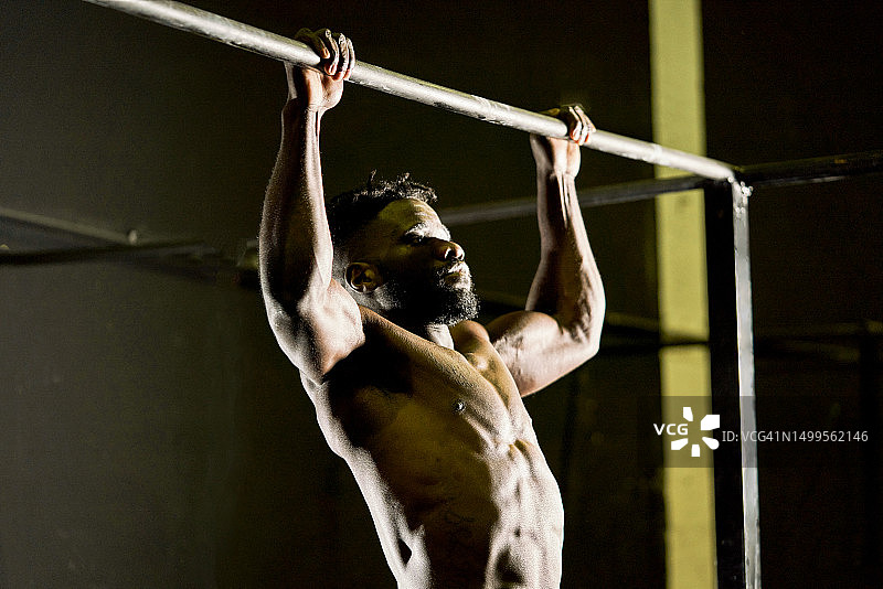 一位健壮的棕色男人专注于在健身房做杠铃俯卧撑的侧面视角图片素材