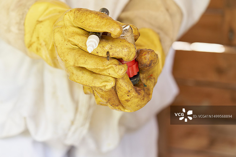 穿着防护服的养蜂人戴着黄色手套的手拿着罐子特写，正面视角图片素材