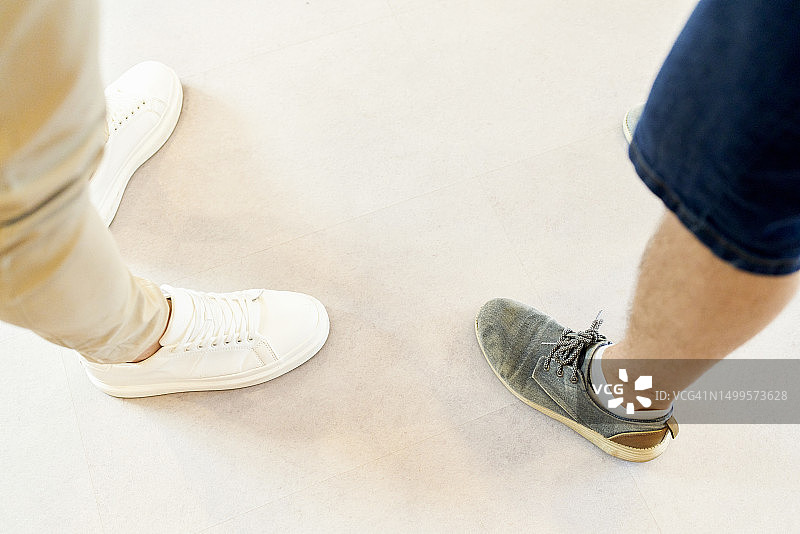 两人站立，一人穿鞋和米色裤子，另一人穿灰色鞋子和蓝色短裤图片素材