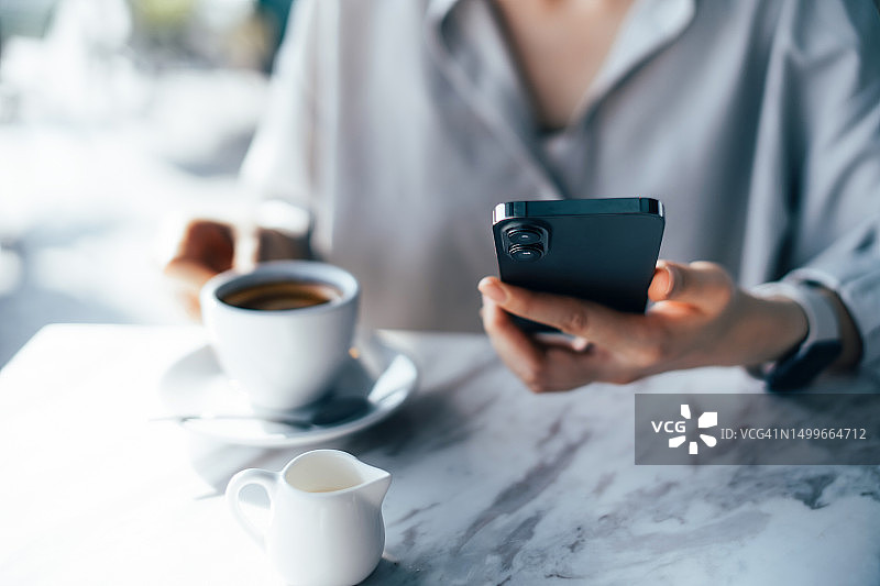 年轻亚洲女子坐在路边咖啡馆喝咖啡并使用智能手机。生活方式与科技图片素材