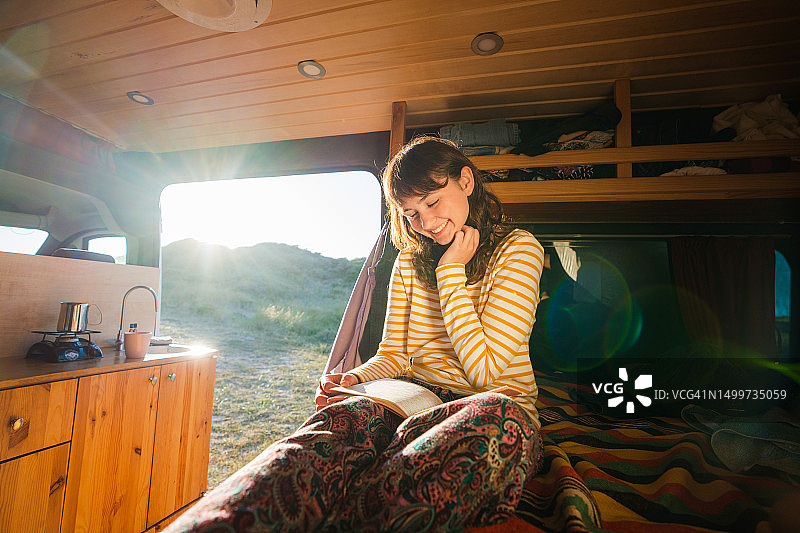 女人在露营车里享受阳光明媚的早晨并阅读图片素材