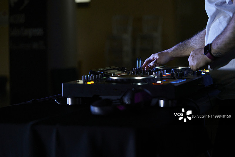 休闲装扮的DJ站在调音台前制作音乐的侧面照，手上戴着手表图片素材