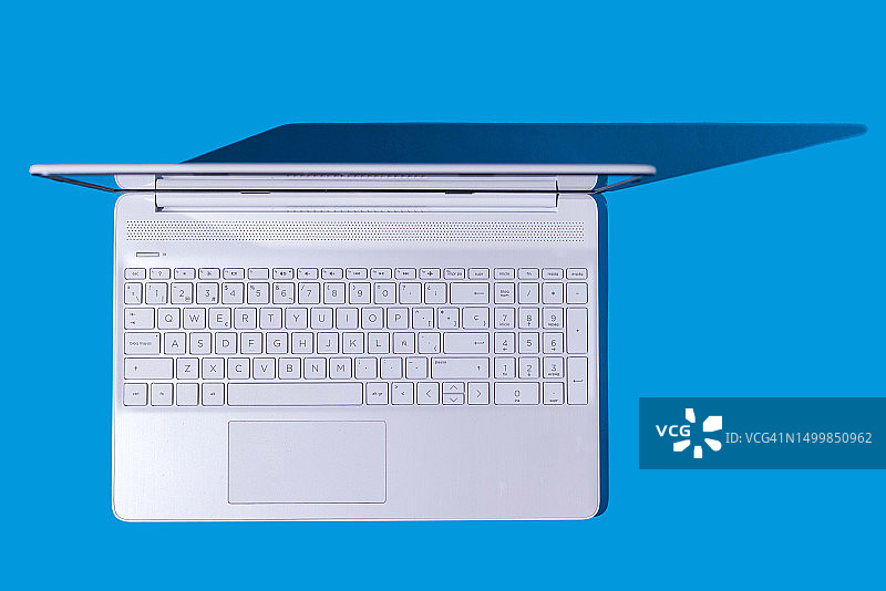 蓝色背景上带有硬阴影的白色笔记本电脑。电脑、互联网、PC、笔记本电脑和远程办公概念图片素材
