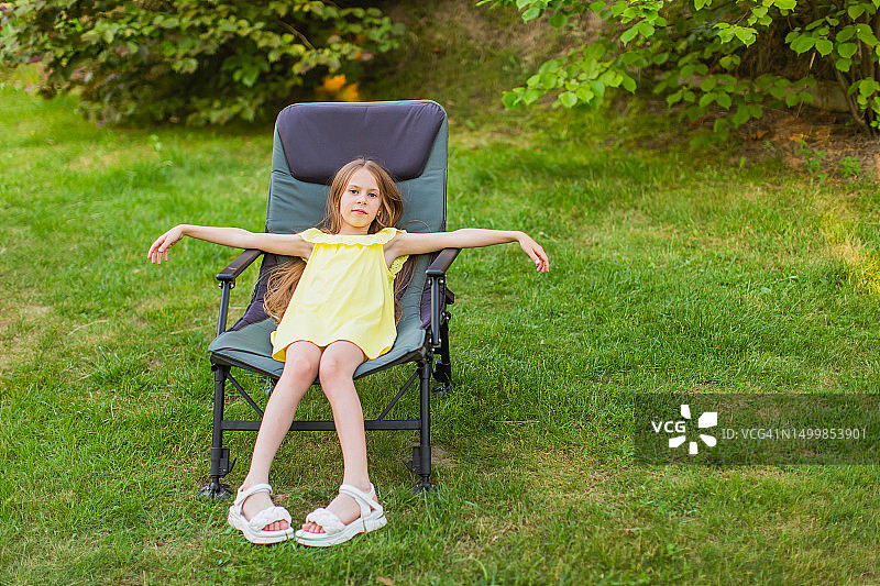 快乐的金发女孩穿着裙子在后院的躺椅上休息。夏日生活，童年。图片素材