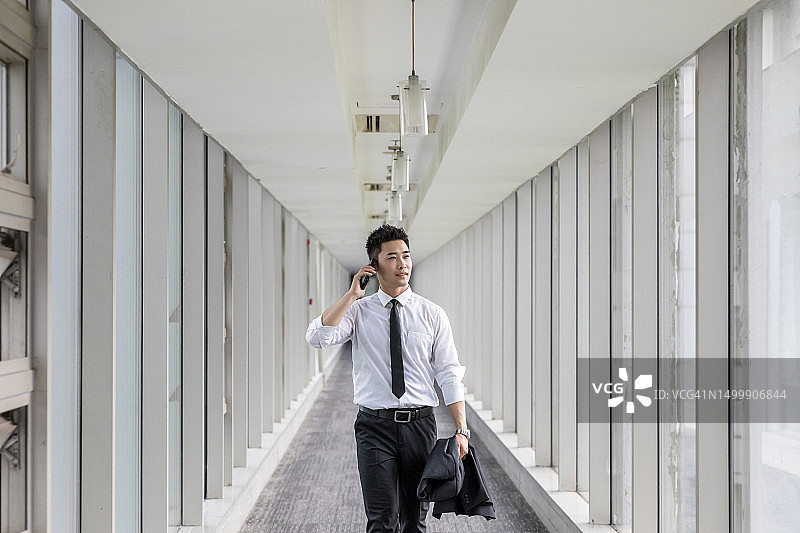 在办公室通道里用手机走路的商人图片素材