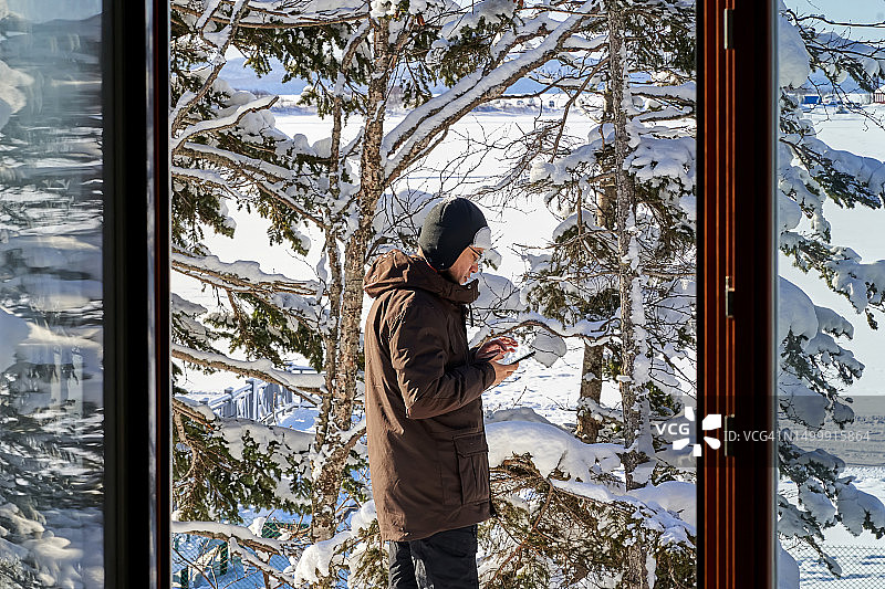 站在窗外，以雪景为背景，看着手机的男人图片素材