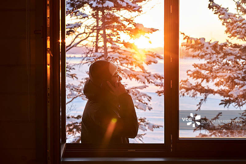 男子站在窗外，以雪景为背景打电话图片素材
