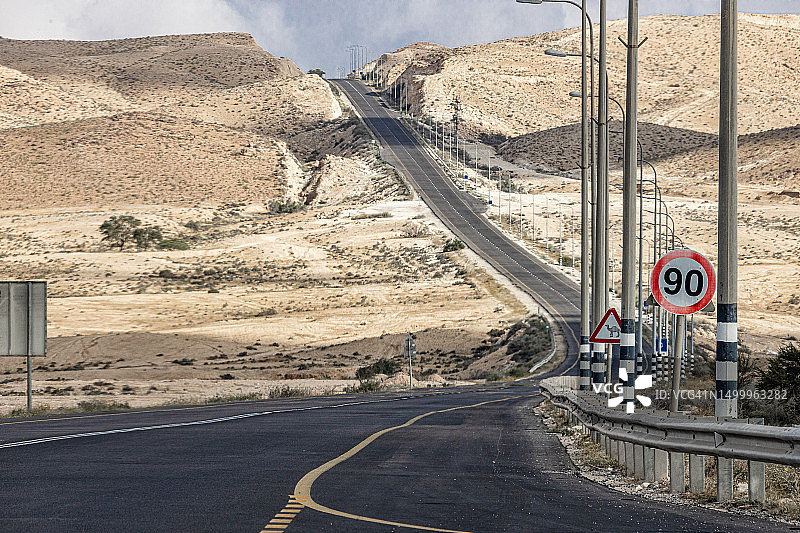 内盖夫沙漠的沥青路，设有路灯和限速标志图片素材