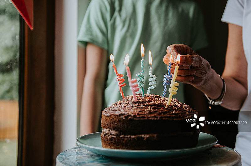 一个女人在生日蛋糕上点燃蜡烛，一个青少年正在观看图片素材