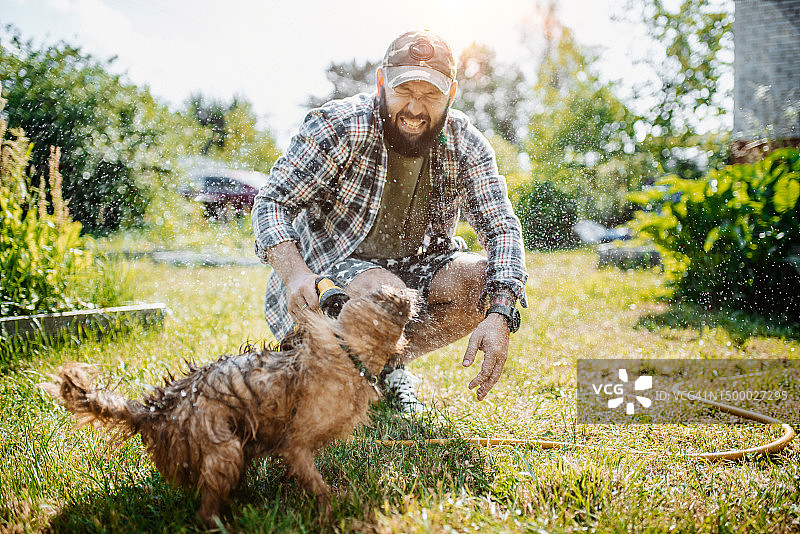 男人在花园里和他的狗一起玩水管图片素材