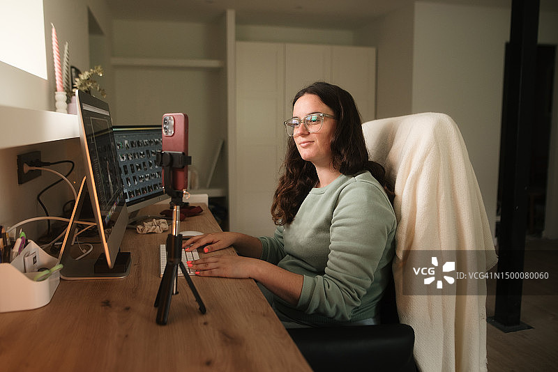 使用电脑和三脚架上智能手机的女人图片素材