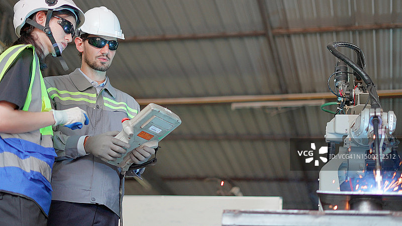 工程师和女技术员使用遥控器控制机器人手臂在工厂焊接图片素材