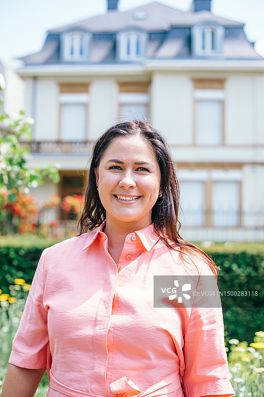 粉色衬衫的中年妇女站在漂亮的房子前图片素材