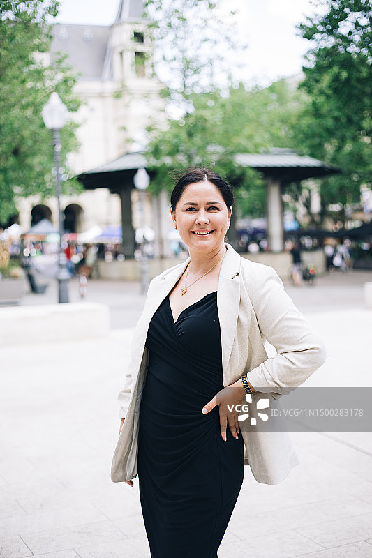 身穿米色西装和黑色连衣裙、凸显身材站在城镇广场的美丽中年女士肖像图片素材
