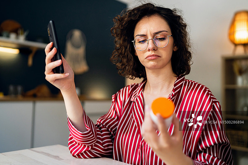 年轻女人拿着药瓶，在智能手机上阅读药品处方图片素材