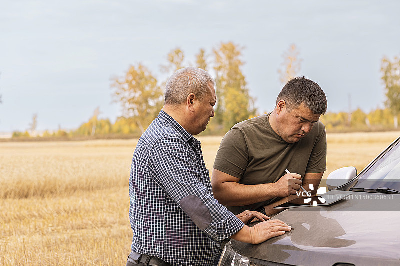 男子在麦田里用平板电脑，父亲在车引擎盖上图片素材