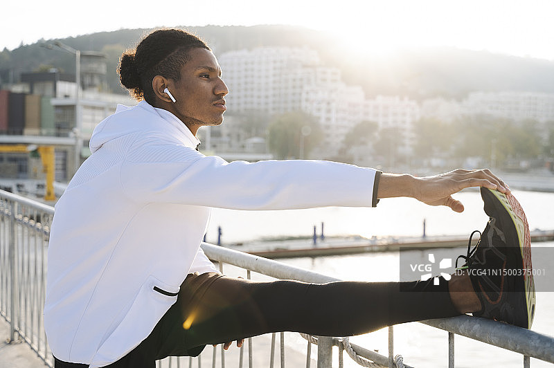戴无线耳机运动员在栏杆附近伸展运动图片素材
