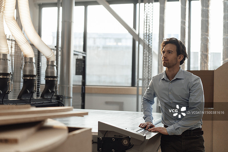 站在工业机械旁的沉思的商人图片素材