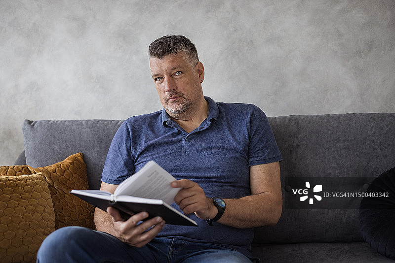男子舒适地坐在家里读书图片素材