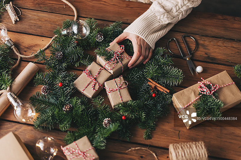 圣诞花环工作坊：在木桌上用手拿着冷杉树枝、松果、浆果、线、剪刀，制作乡村圣诞花环图片素材