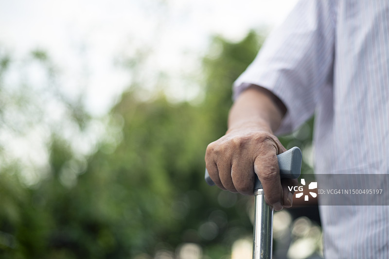 特写：老人戴着手表，拄着拐杖站在房子前图片素材