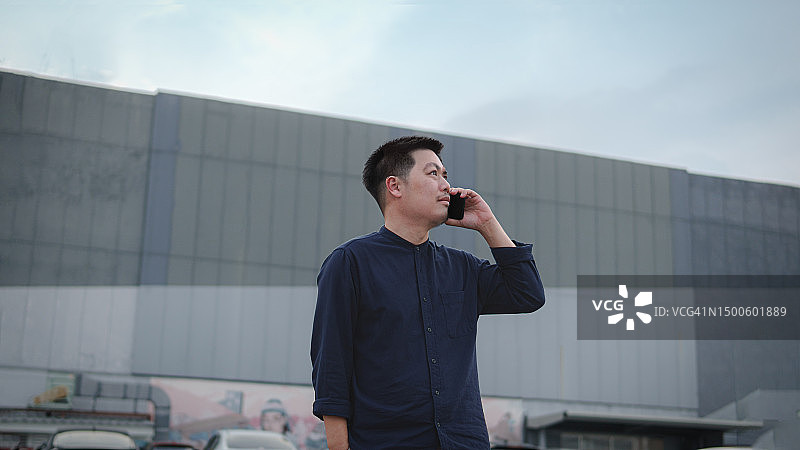 亚洲商人使用智能手机的自信和成功的生活方式，该男子站在城市的摩天大楼前。健康与商业领导力。通过摩天大楼城市的数字连接拥抱生活方式和商业。图片素材