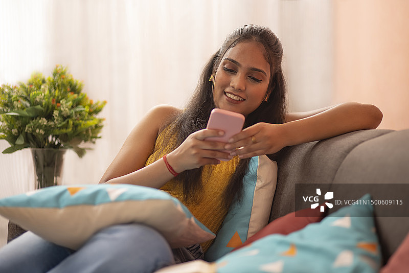 年轻女子在客厅沙发上放松，用手机阅读信息图片素材
