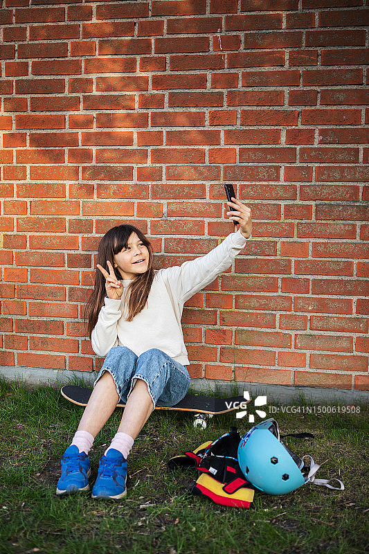 年轻女孩坐在滑板上用手机自拍图片素材