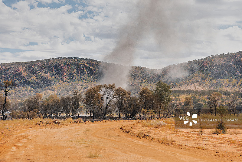 从土路拍摄的在树木中盘旋的尘卷风，澳大利亚北部地区塔纳米沙漠图片素材