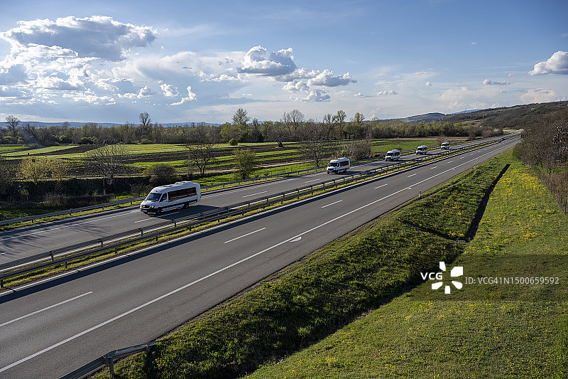 在高速公路上快速行驶到城市郊区的白色现代送货小型货物快递车。行驶在高速公路上的白色现代舒适旅游巴士。旅游和长途汽车旅游概念图片素材
