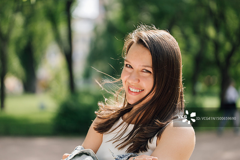 站在公园里，看着相机的长棕色头发的微笑女人图片素材