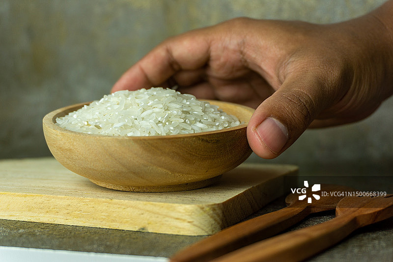 手持装在木碗里的未煮熟的稻米或干米（配有木勺和叉子，塞尔维亚）图片素材
