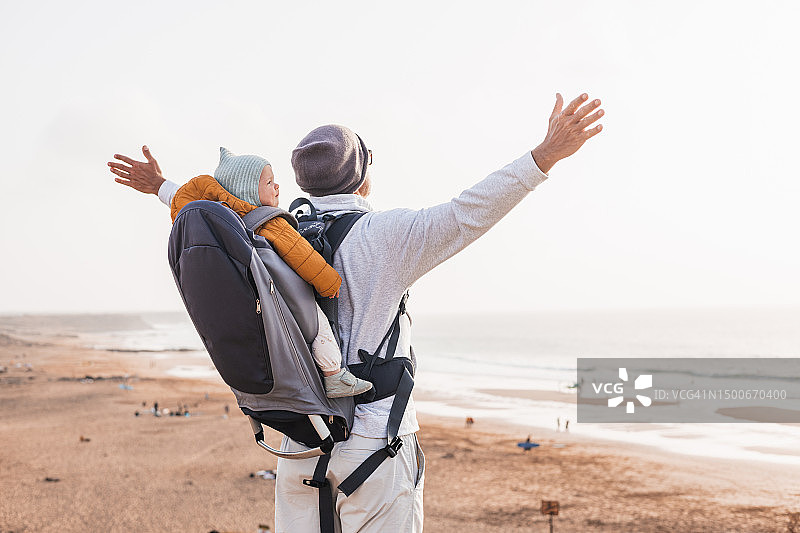 年轻的父亲背着宝宝，在户外享受大自然图片素材