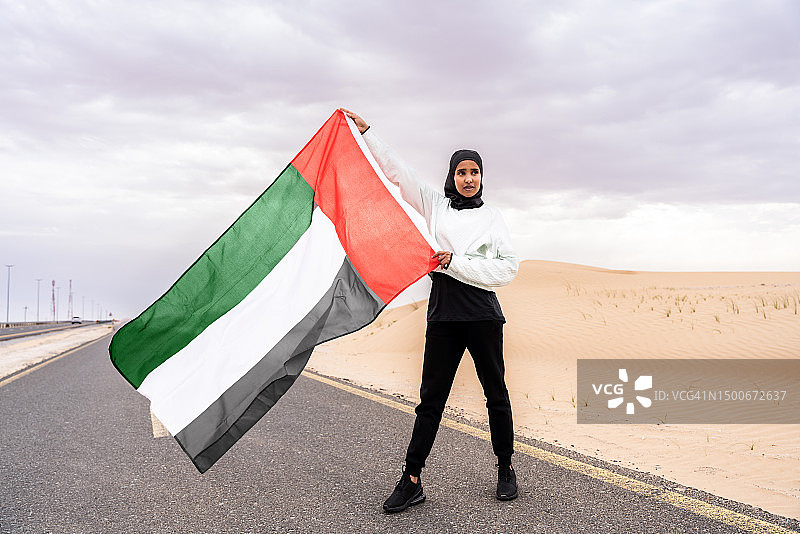 阿拉伯运动女性戴着头巾在户外训练，手持阿联酋国旗，阿拉伯联合酋长国图片素材