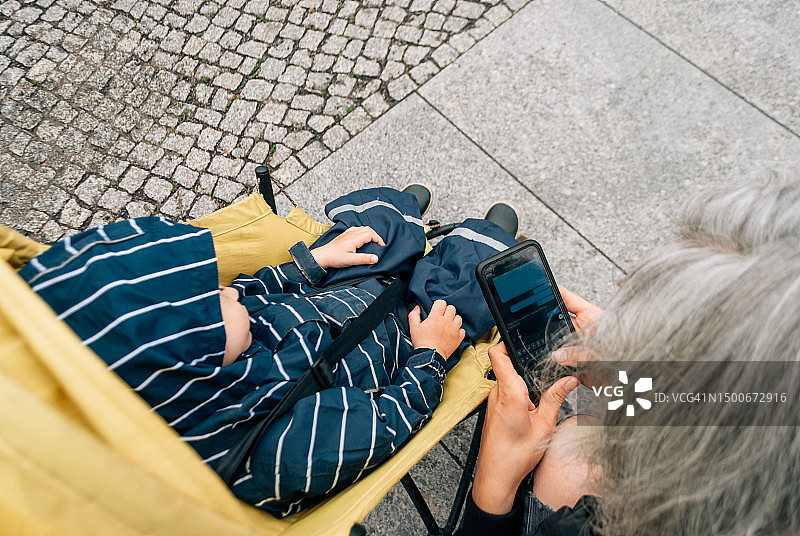 俯视图，一个女人在她的手机上输入信息，靠近一个带着孩子的婴儿车，德国图片素材