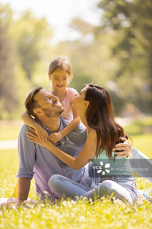 幸福的年轻家庭和可爱的女儿在阳光明媚的公园里玩耍图片素材