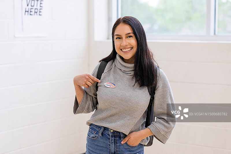 快乐的年轻女人自豪地指着“我投票了”贴纸图片素材