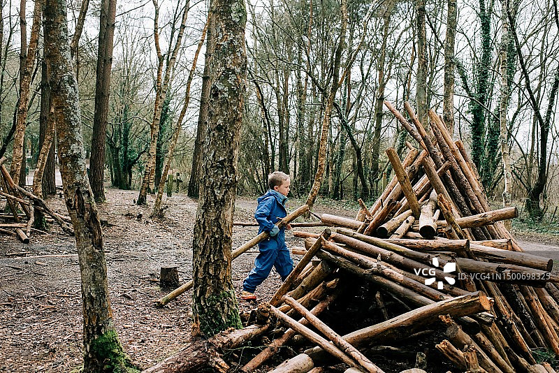 金发小男孩在森林里搬运木头搭建小屋图片素材