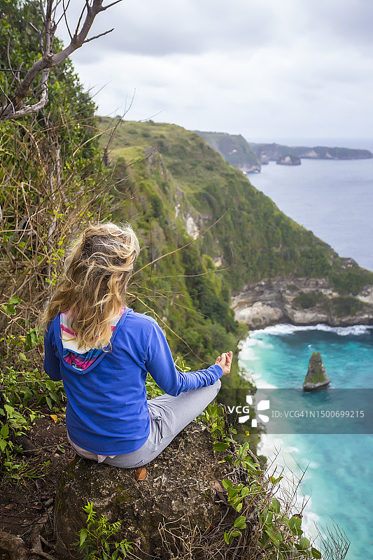 在印度尼西亚巴厘岛海岸悬崖边冥想的金发女子图片素材