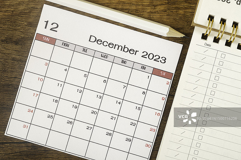2023年桌面日历：十二月是组织者计划和截止日期的月份，木质背景上的白色铅笔和清单纸图片素材