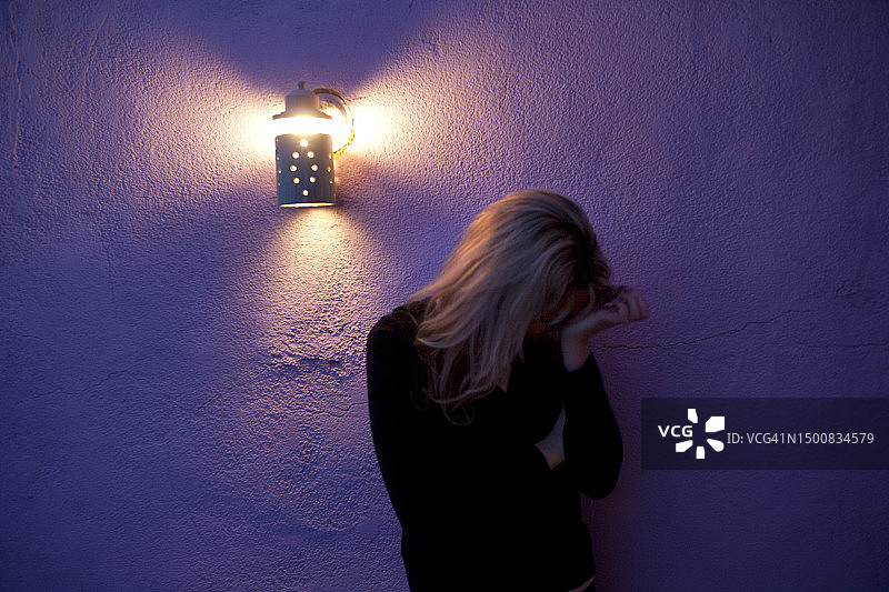 女人双手抱头，夜晚站在紫色墙壁前图片素材