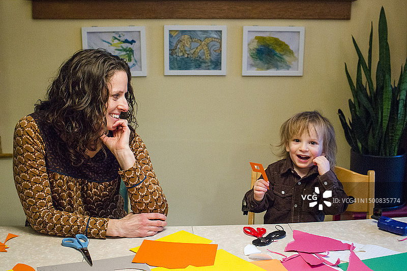 面带微笑的母亲和小儿子在餐桌上一起创作艺术作品图片素材