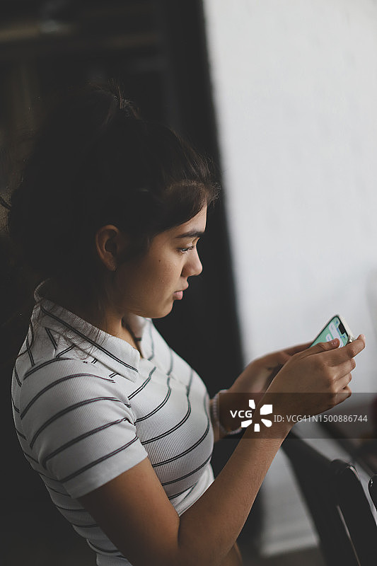 女孩在家坐在椅子上使用手机的侧面图图片素材
