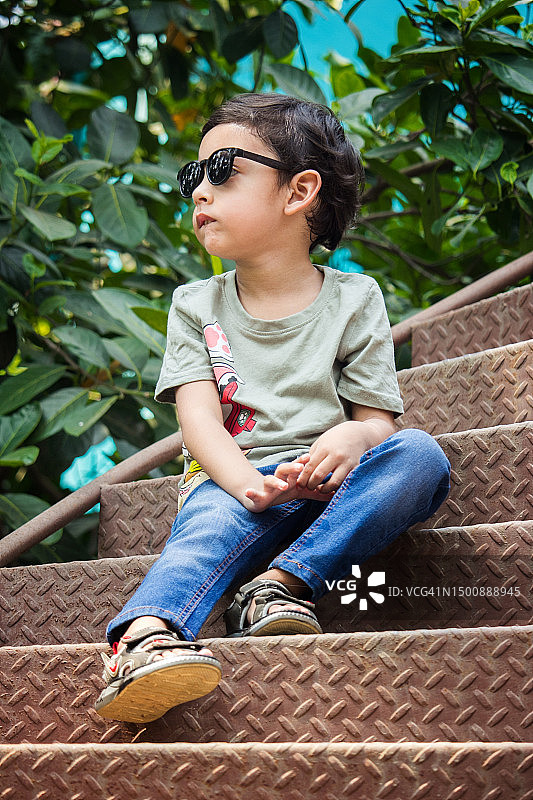 戴着太阳镜坐在楼梯上的可爱男孩，孟加拉国图片素材
