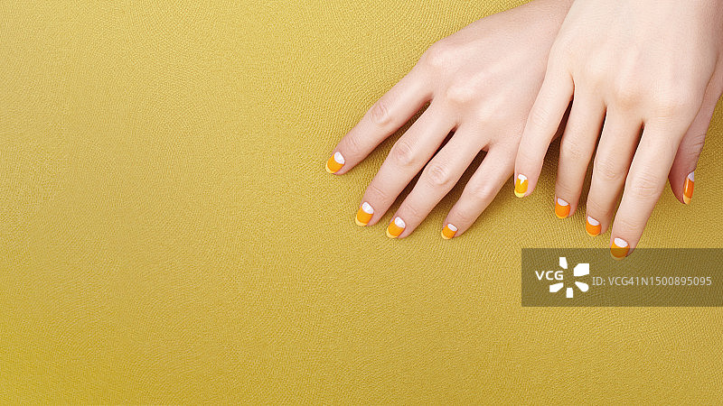 在黄色背景上有着鲜艳橙色糖果玉米美甲的美丽女性的手图片素材