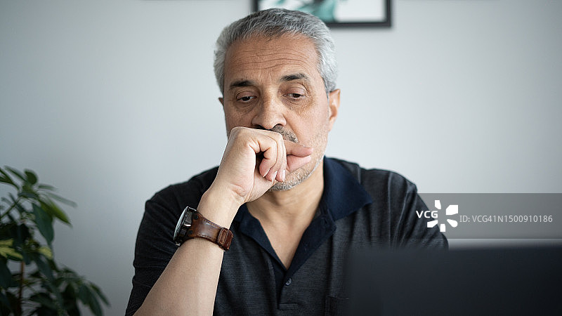 在家工作，看着笔记本电脑陷入沉思的成年男人图片素材