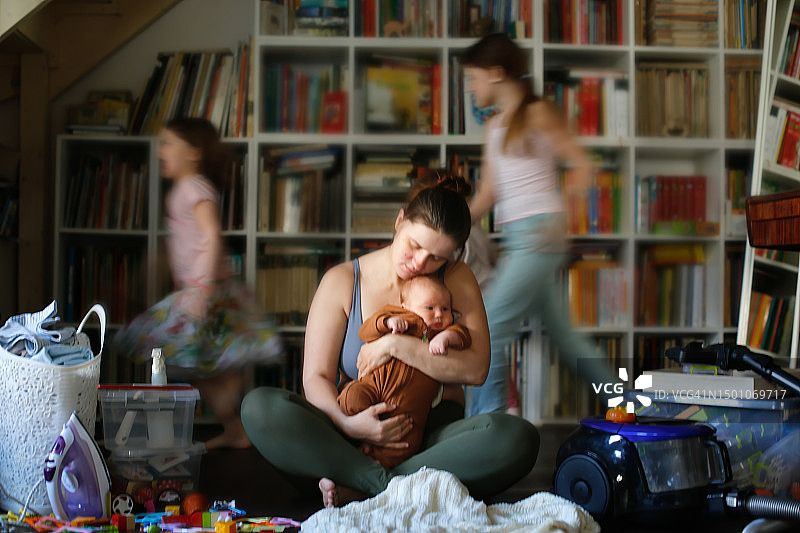 母爱忧郁：在客厅里不堪重负的母亲和模糊跑动的孩子图片素材